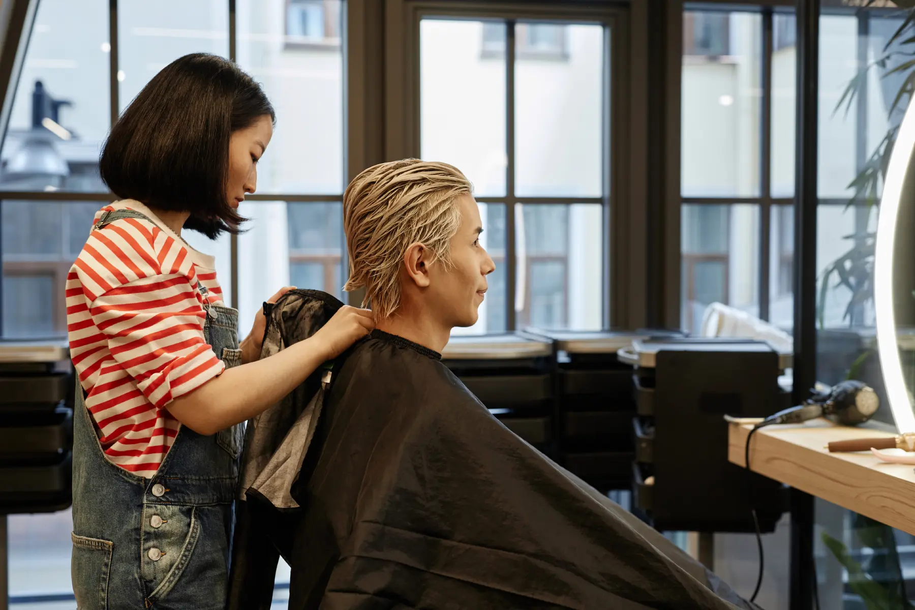 young-hairstylist-putting-protective-cape-on-male-2026-03-19-10-42-14-utc